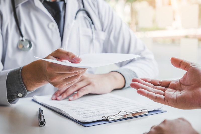 Un médecin qui tends un papier à un patient en consultation 