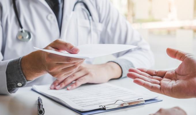 Un médecin qui tends un papier à un patient en consultation 