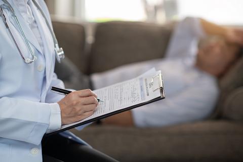 un médecin qui prend des notes pendant une consultation avec un patient qui est allongé 