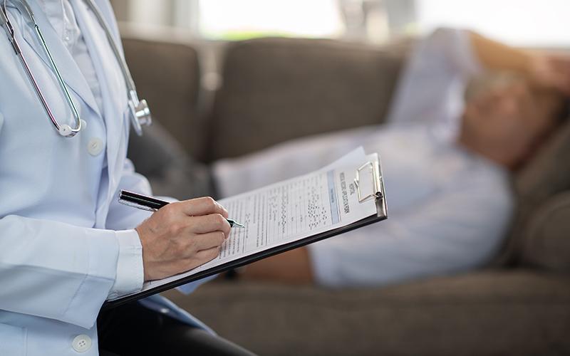 un médecin qui prend des notes pendant une consultation avec un patient qui est allongé 